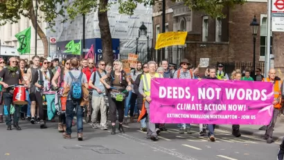 A group of protests with signs and drums walk down the street.